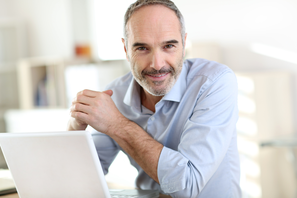 homem sorrindo com notebook branco