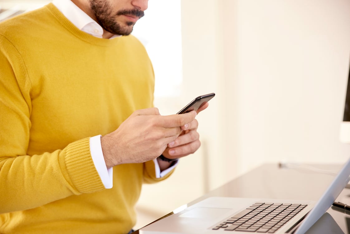 homem usando celular em frente ao computador