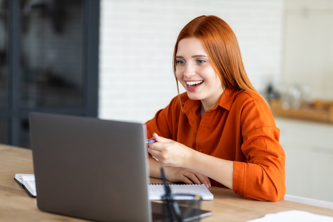 mulher ruiva sorrindo e olhando um notebook