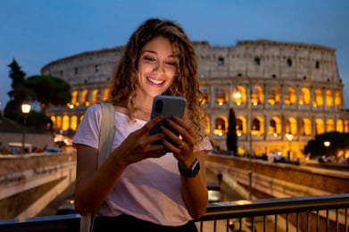 mulher de noite sorrindo com celular com o coliseu romano ao fundo