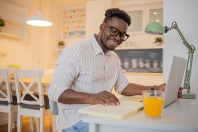 Homem em casa sorrindo lendo caderno e usando computador