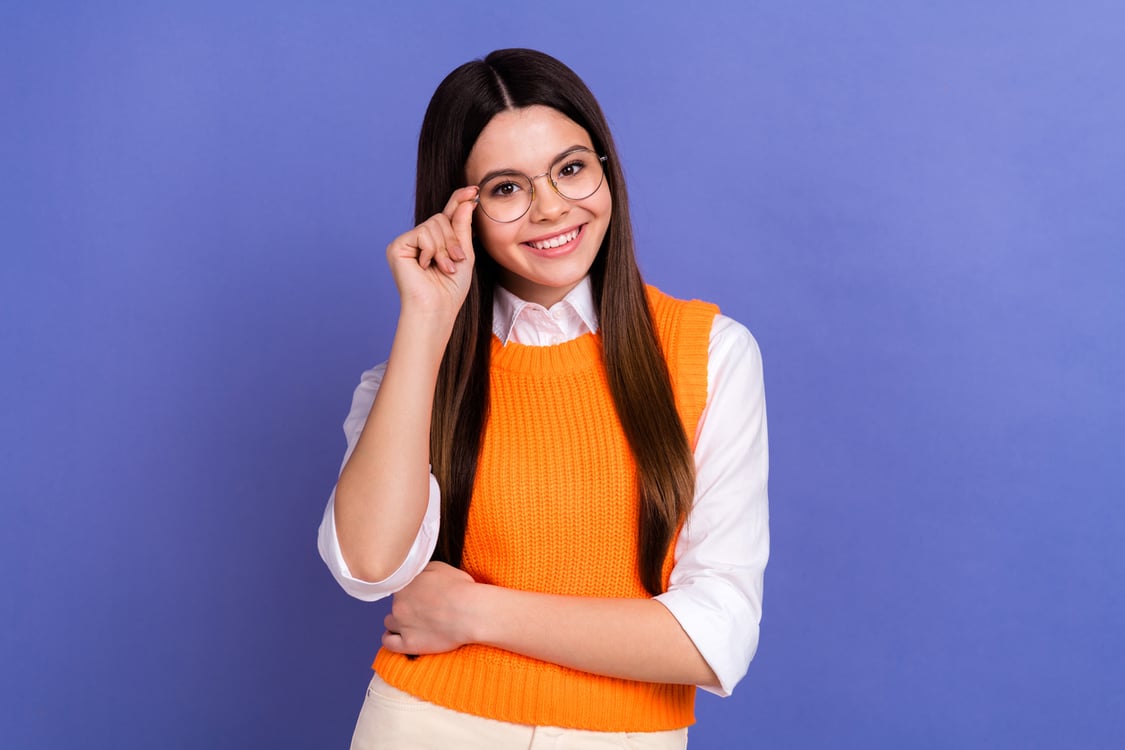 mulher sorrindo segurando óculos no fundo roxo