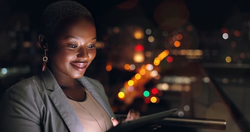 Mulher usando um tablet no escuro com uma cidade ao fundo