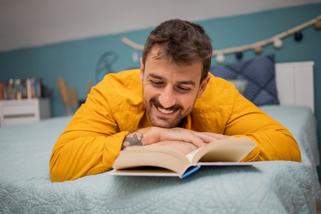 homem lendo livro em cima da cama