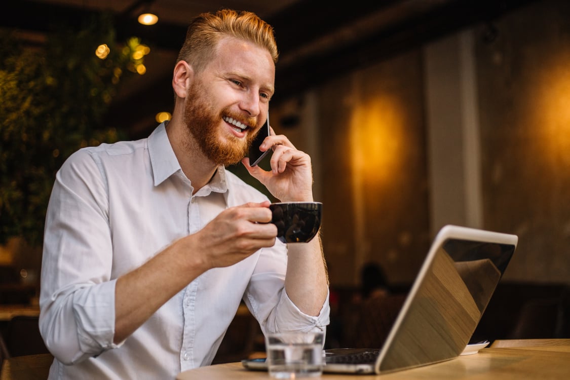 homem ruivo com notebook e café na mão